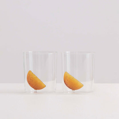 Two clear glass goblets with a playful amber-hued citrus slice design nestled in the base, displayed against a white background.